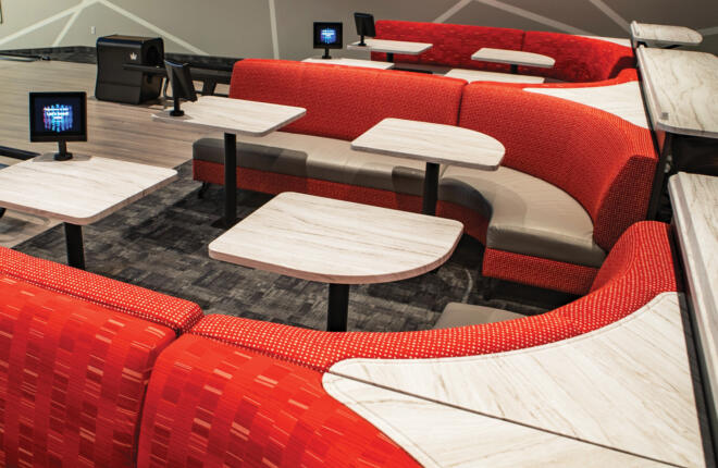 Curved red seats with white tables and screens in modern space.