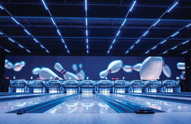 Wide view of modern bowling lanes with LED ceiling lighting, glossy lanes, and a large digital video wall.