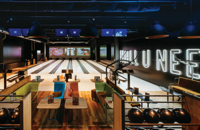Overhead view of modern bowling lanes with colorful seating, menu tables, and large-format digital displays.