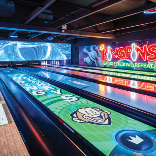 Bowling lanes with digital displays, neon KingPins logo, and Spark projections