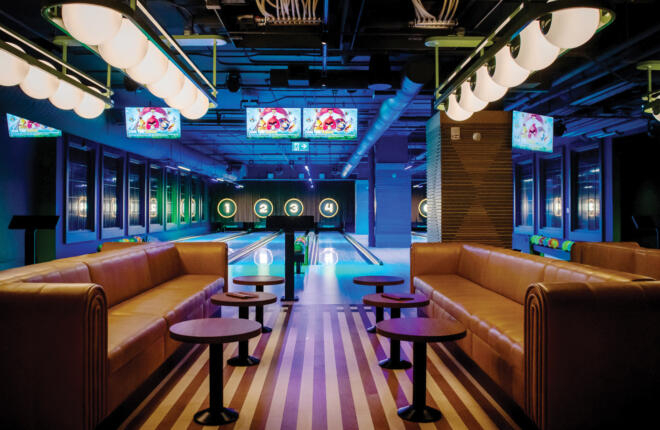 Modern bowling alley with brown leather couches, striped floor, colorful screens