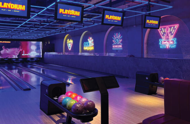 Neon-lit bowling alley with colorful balls and screens showing 'PLAYDIUM' and a movie scene.