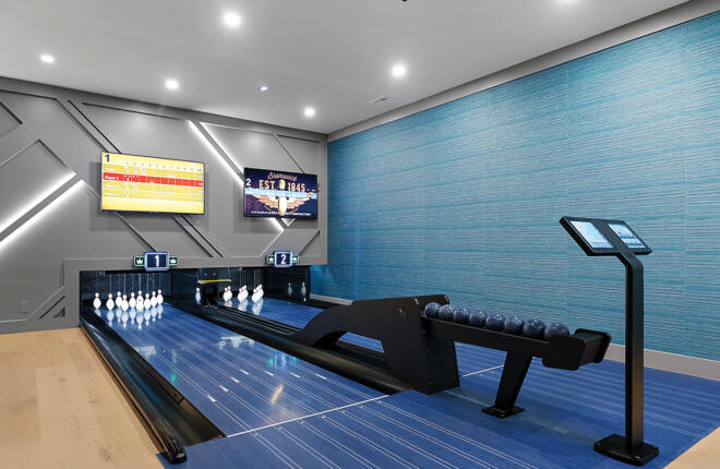 Close-up view of a two-lane residential bowling setup with Brunswick Sync scoring screens, illuminated pin decks, and sleek geometric wall lighting.