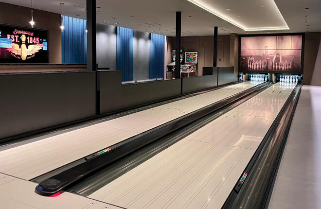 Modern bowling alley with two lanes, vintage mural masking units, digital scoreboard, and blue wall panels.