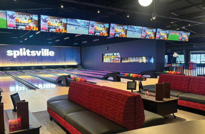 Bowling alley with colorful balls, large screens, and red cushioned benches.