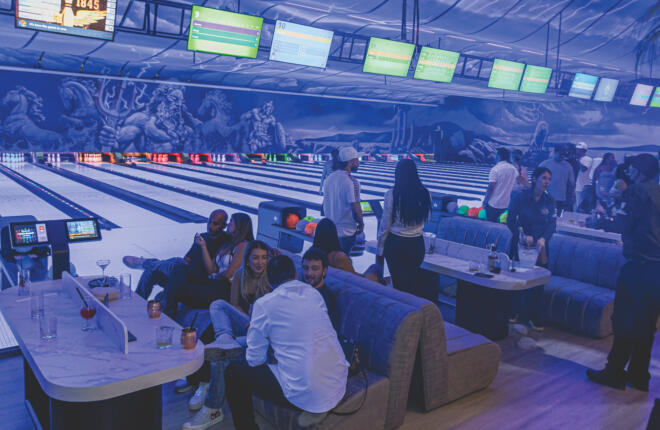 People socializing and bowling in a modern bowling alley with neon lights.