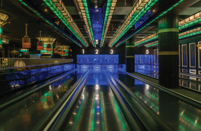 Five-lane boutique bowling alley with illuminated green ceiling panels and reflective lanes in a high-end venue.