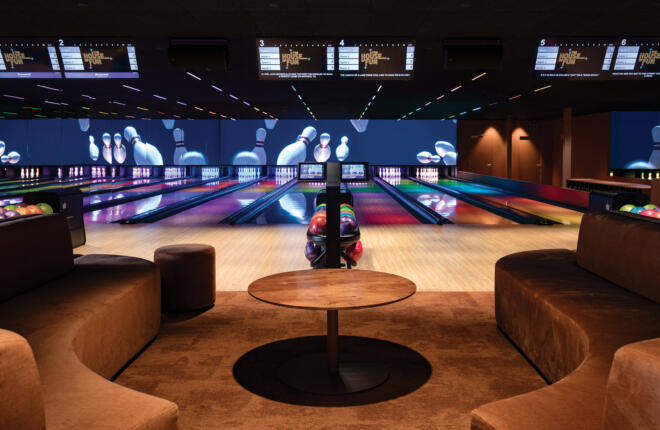 High-end bowling lanes with immersive LED video wall, vibrant lane lighting, and comfortable lounge seating for social play.