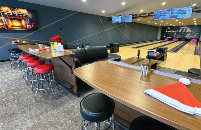 Home bowling lanes with seating, a Santa hat on a table, and a fireplace screen.