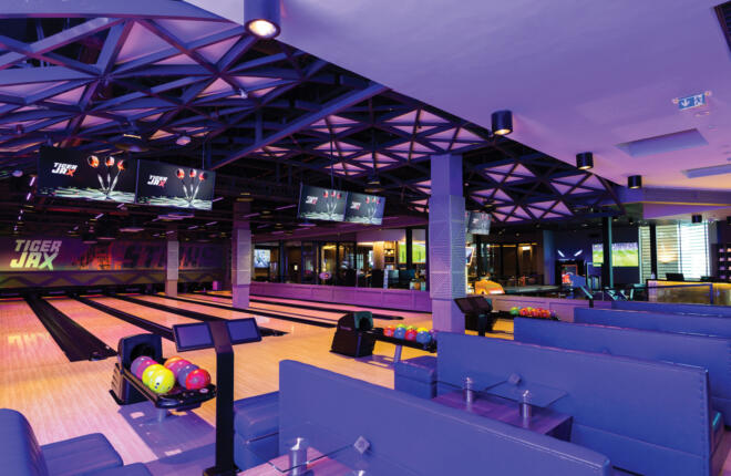 Modern bowling lanes with colorful balls, blue seating, and purple lighting.