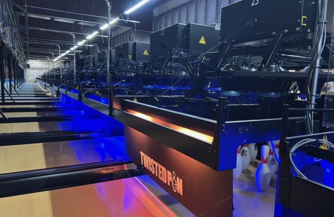 Row of "TWISTED PIN" branded pinsetter units with orange lighting and blue-lit lanes, bowling pins set at the nearest lane, numbered machine panels visible above.