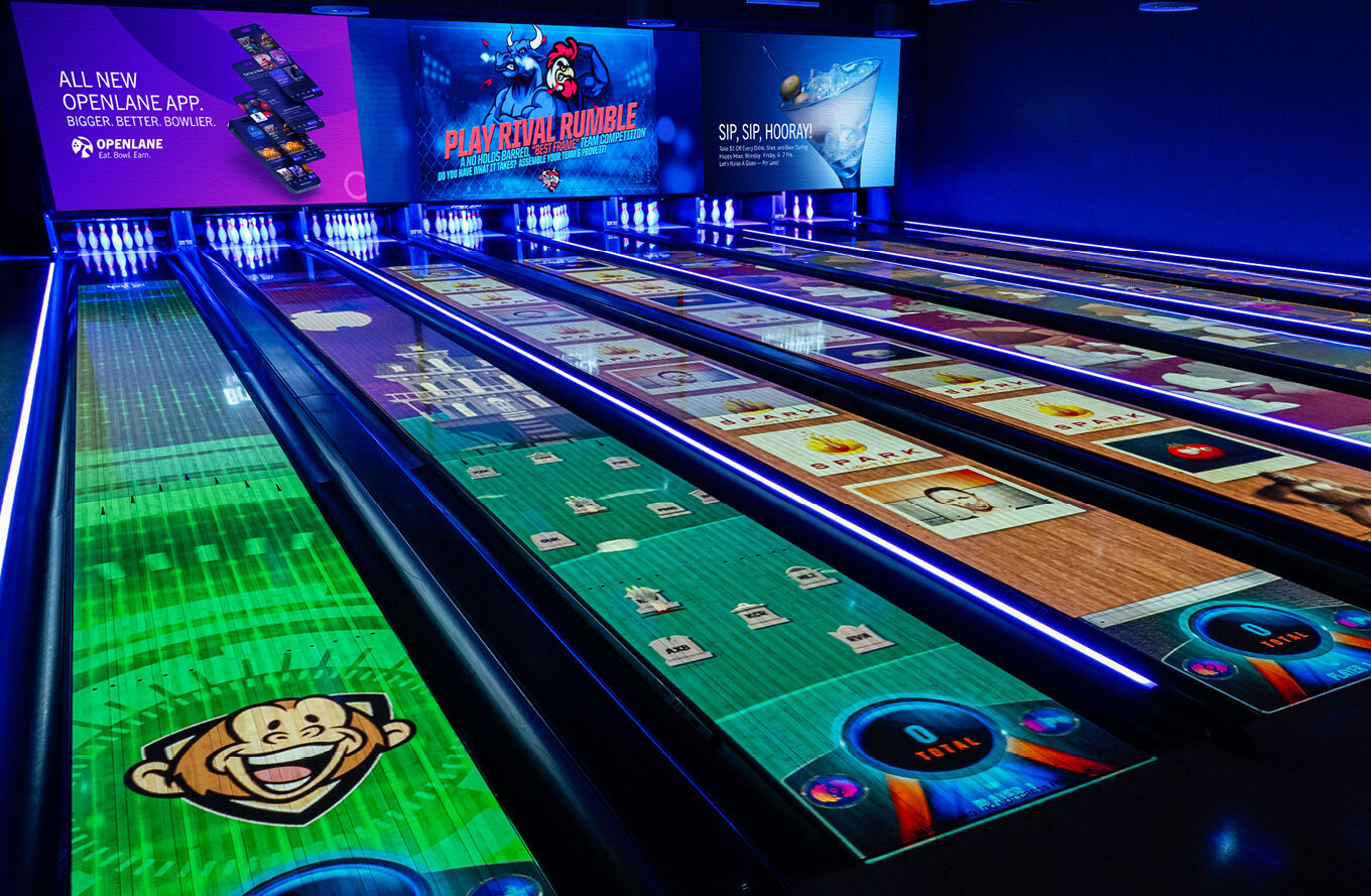 Modern bowling alley with digital displays on lanes and blue lighting.