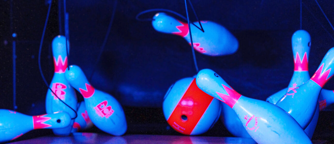 A bowling ball collides with blue Boost ST string pins, captured mid-motion under neon lighting.