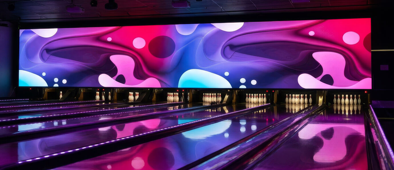 Brunswick LED Video Wall displaying a fluid abstract design with swirling purple, pink, and blue shapes accented by floating circular elements, stretched across the back wall above illuminated bowling lanes and pin decks.