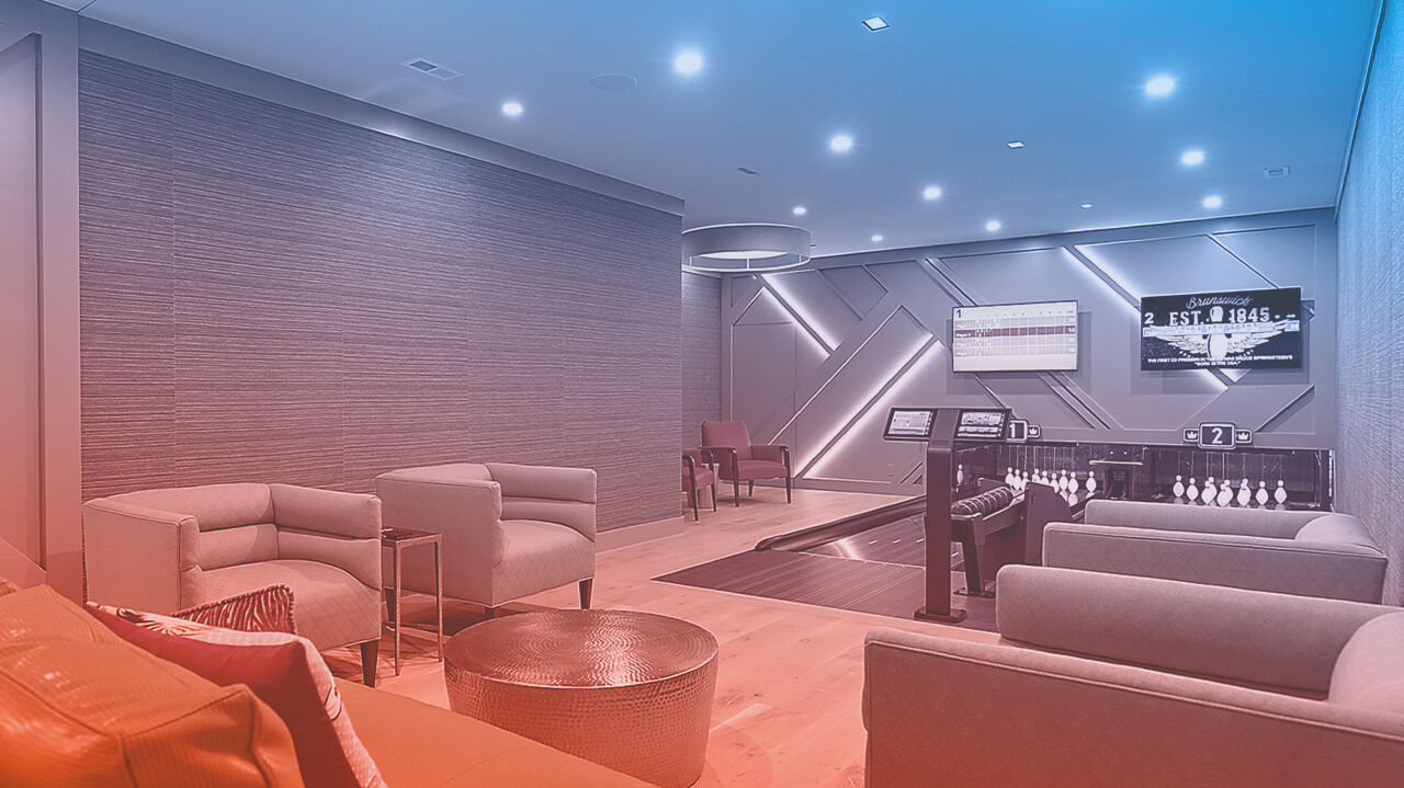 Elegantly designed private Duckpin Social bowling lounge featuring two Brunswick lanes with scoring consoles, upholstered lounge seating, hardwood floors, and geometric LED wall accents. Brunswick "Est. 1845" branding displayed on overhead screens.