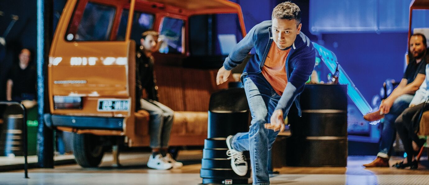 Man ready to bowl, poised at lane in lively bowling alley atmosphere.