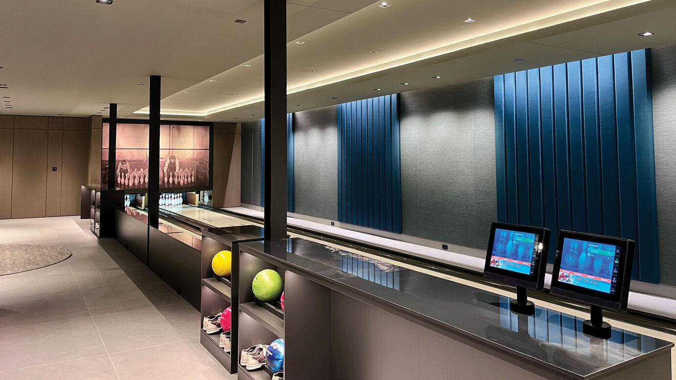 Modern bowling alley with two lanes, colorful balls on shelves, digital screens, and blue panel walls.
